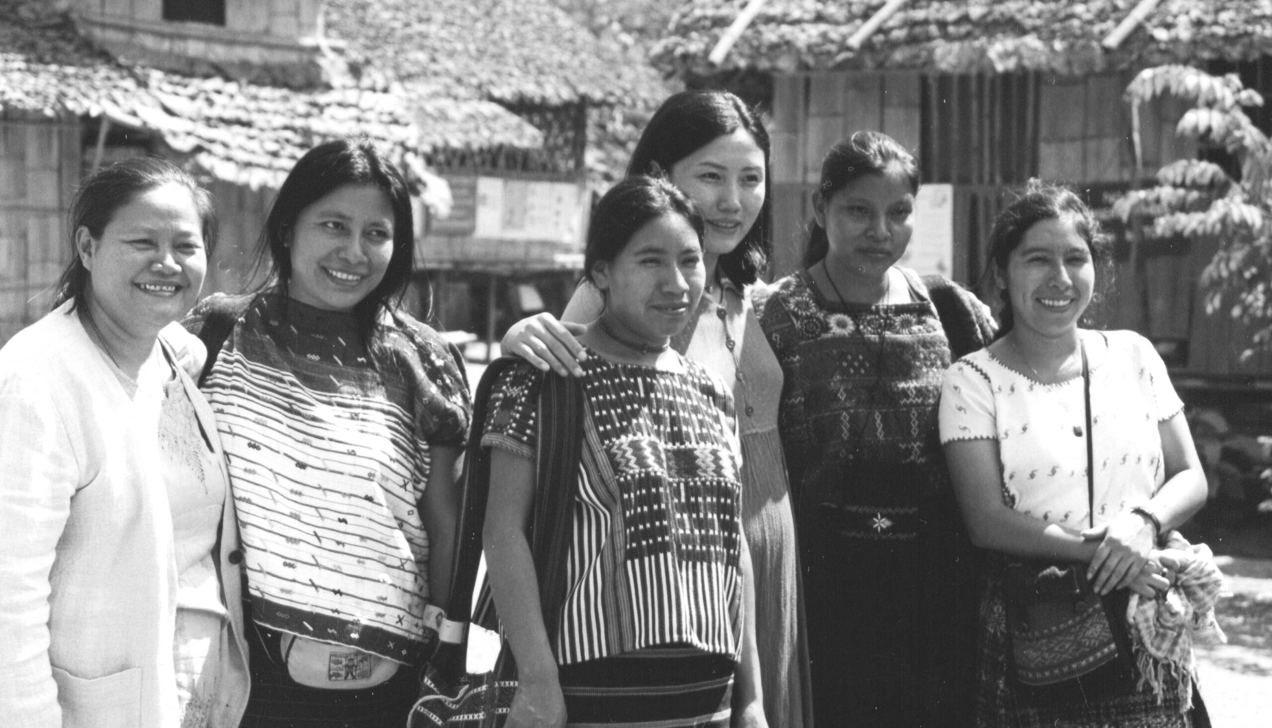 A black and white photo shows women from Burma and Guatemala standing together, with houses in the background.